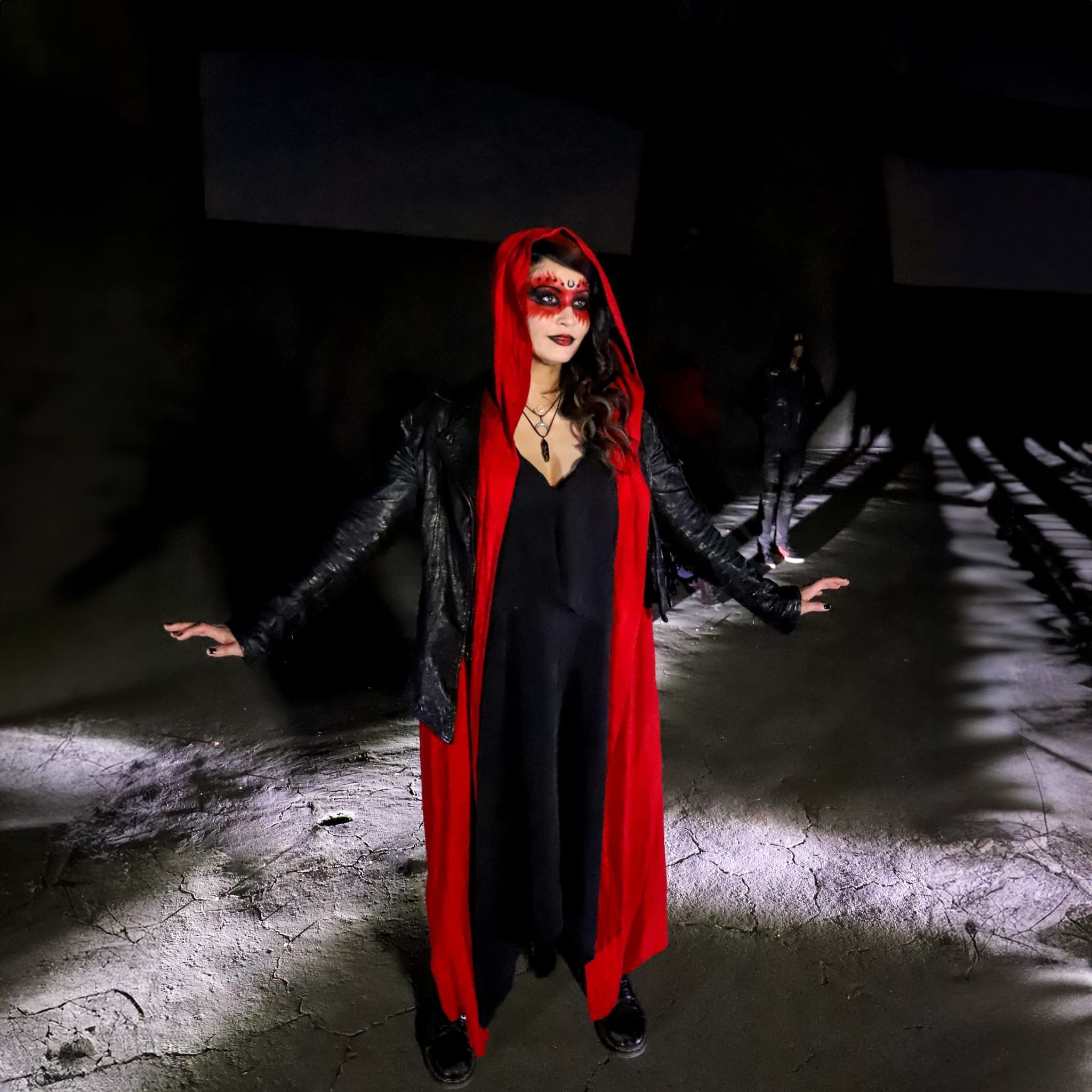 Tash performing in red cloak, dark industrial setting